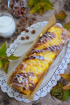 a long pastry with icing sitting on top of a doily next to some nuts