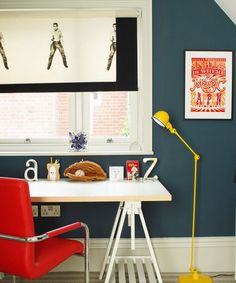 a red chair sits in front of a white desk with a yellow lamp on it