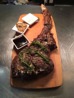 a wooden cutting board topped with meat and dipping sauces on top of a table