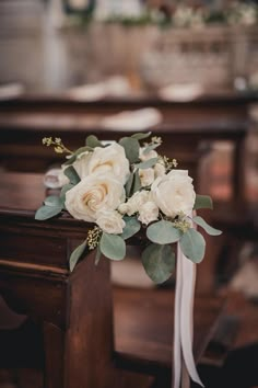 a bouquet of white roses and greenery sits on the pew at a wedding ceremony