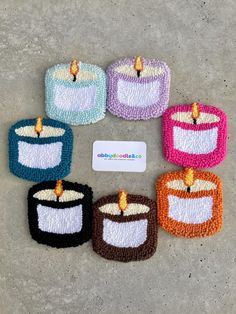 six small crocheted candles sitting next to each other on the cement floor with a business card in front of them