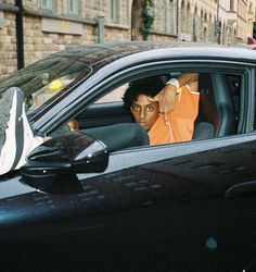 a man sitting in the driver's seat of a car with his hand up