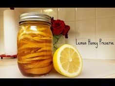 a mason jar filled with lemon honey preserver next to a sliced lemon and red rose