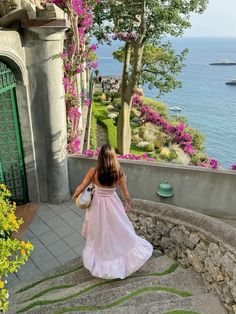 a woman in a pink dress is walking up the stairs to an entrance with flowers on it