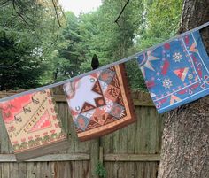 three colorful blankets hanging on a clothes line next to a tree in a backyard area