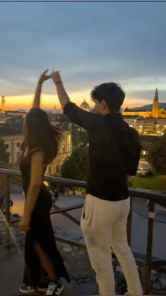 a man and woman standing on top of a roof with their arms in the air