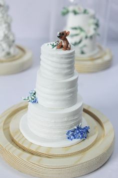 three tiered wedding cake with small figurines on each layer and blue flowers