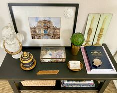 a black table topped with books and vases next to a framed photograph on the wall