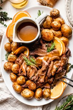 a plate full of roast, potatoes and gravy with orange slices on the side