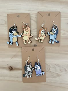 three cartoon keychains are shown on a wooden surface, one has a cat and the other has a dog