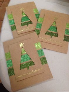 three brown christmas cards with green glitter trees on them, sitting on a white table