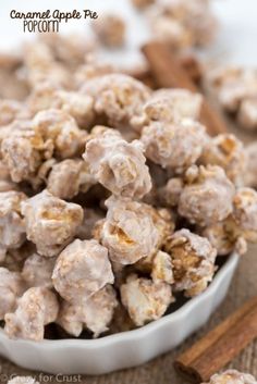 a white bowl filled with caramel popcorn next to cinnamon sticks