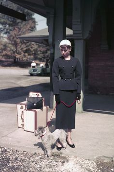 a woman is standing on the sidewalk with her dog and suitcases in front of her