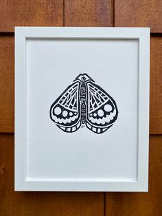 a black and white drawing of a moth in a frame on a wooden wall with wood paneling