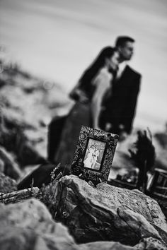 a couple standing next to each other on rocks with a frame in the foreground