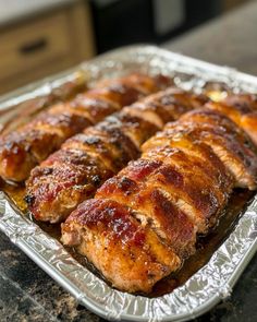 meat wrapped in tinfoil sitting on top of a metal pan filled with sauce and ketchup