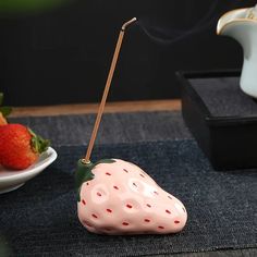 a strawberry shaped incense burner sitting on top of a table next to a bowl of strawberries