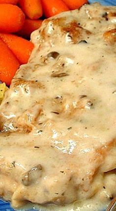 a blue plate topped with meat covered in gravy next to carrots and potatoes