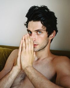 a shirtless man with his hands folded over his chest and eyes closed while sitting on a couch