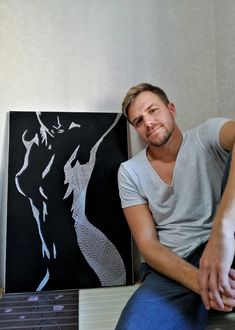 a man sitting next to a black and white painting