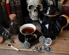 a cup of tea next to some silverware and books on a wooden table with skulls in the background