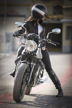 a woman in black riding on the back of a motorcycle