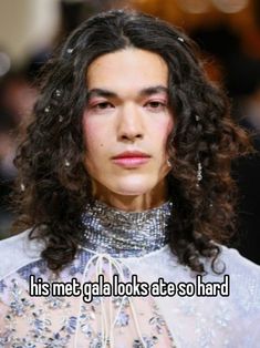 a man with long curly hair wearing a white shirt and silver jewelry on his neck