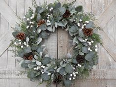 a wreath with white berries and greenery is hung on a wooden door, surrounded by pine cones