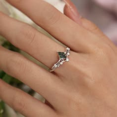 a woman's hand with a ring on top of it and flowers in the background