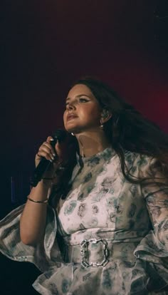 a woman holding a microphone in her right hand and wearing a dress with flowers on it