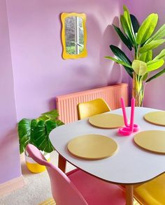 a dining room with pink and yellow chairs, a potted plant on the table