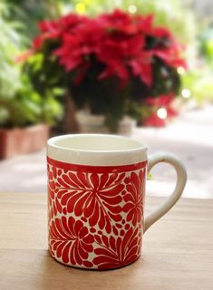 a red and white coffee cup sitting on top of a wooden table next to a potted plant