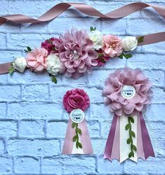 pink and white paper flowers are hanging on a brick wall next to ribbons with name tags