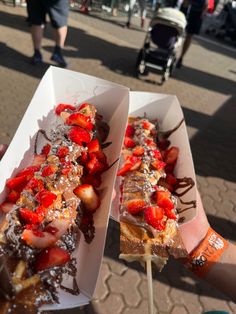 someone is holding two desserts with strawberries and chocolate on them in their hands