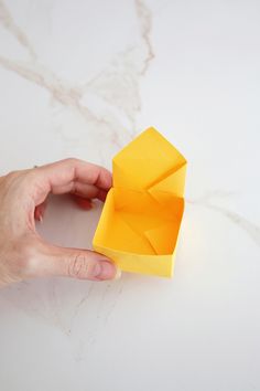 a hand holding an origami object on top of a white table with marble