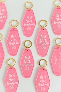 nine pink key chains with white writing on them that say be a nice human and be a nice human