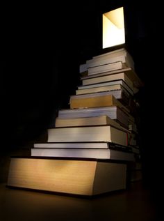 a stack of books sitting on top of a wooden table next to a light bulb