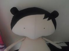 a white stuffed animal with black hair and eyes sitting on top of a table next to a wall