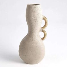 a white ceramic vase with two handles on the top and bottom, sitting in front of a white background