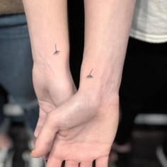 two people holding hands with small tattoos on their arms and one is holding the other's hand