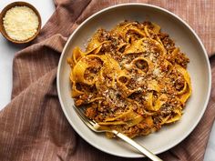 a white bowl filled with pasta and meat on top of a brown cloth next to a wooden spoon