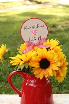 sunflowers are in a red pitcher with a sign