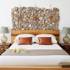 a bed with two lamps on each side and a stone wall behind the headboard