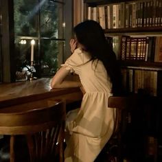 a woman sitting at a wooden table in front of a book shelf filled with books