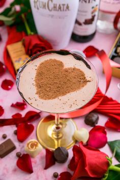 a drink in a wine glass with a heart on the rim surrounded by roses and chocolates