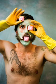 a shirtless man wearing yellow rubber gloves holds his hands up to his face as he covers his eyes