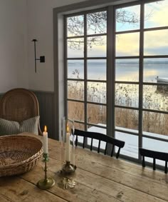 a wooden table with candles on it in front of a large window overlooking the water