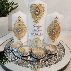 the wedding candles are decorated with gold and silver designs on white frosted glass plates