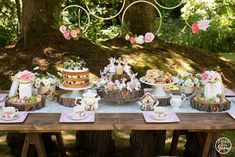 an outdoor picnic table set up with tea cups, cakes and desserts