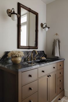 a bathroom vanity with marble counter top and gold faucet, mirror above it